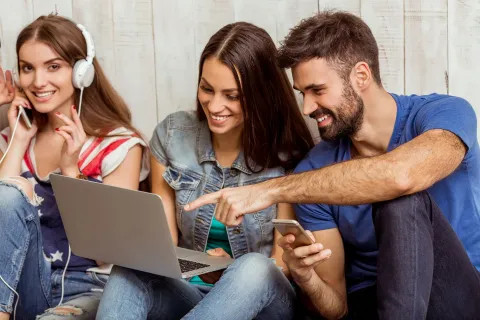 Tři mladí přátelé se dívají do notebooku a telefonu