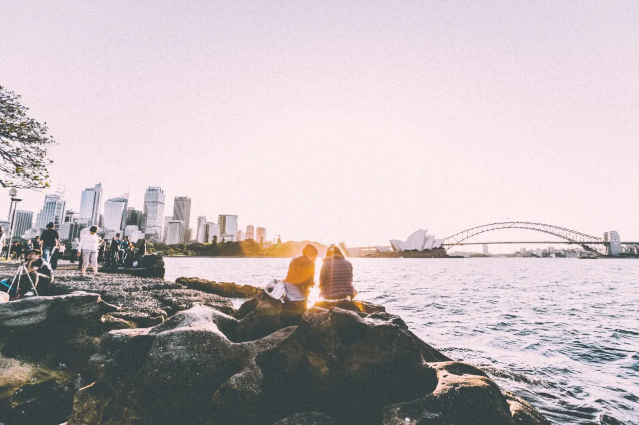 People relaxing on the rocks by Sydney Harbour, with the city skyline in the distance
