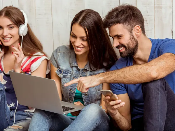 Three young friends sharing a laptop and a phone