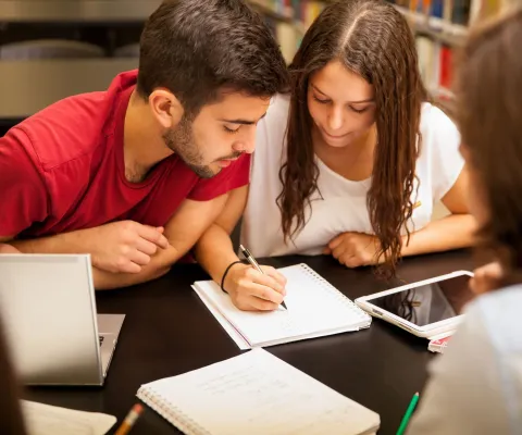 Studenti společně procházejí poznámky u stolu v knihovně